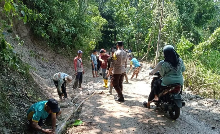 ANGGOTA POLSEK CIBUGEL GOTONG ROYONG DENGAN WARGA BERSIHKAN SISA MATERIAL LONGSOR